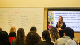 A woman presenting to room with a slide show behind her